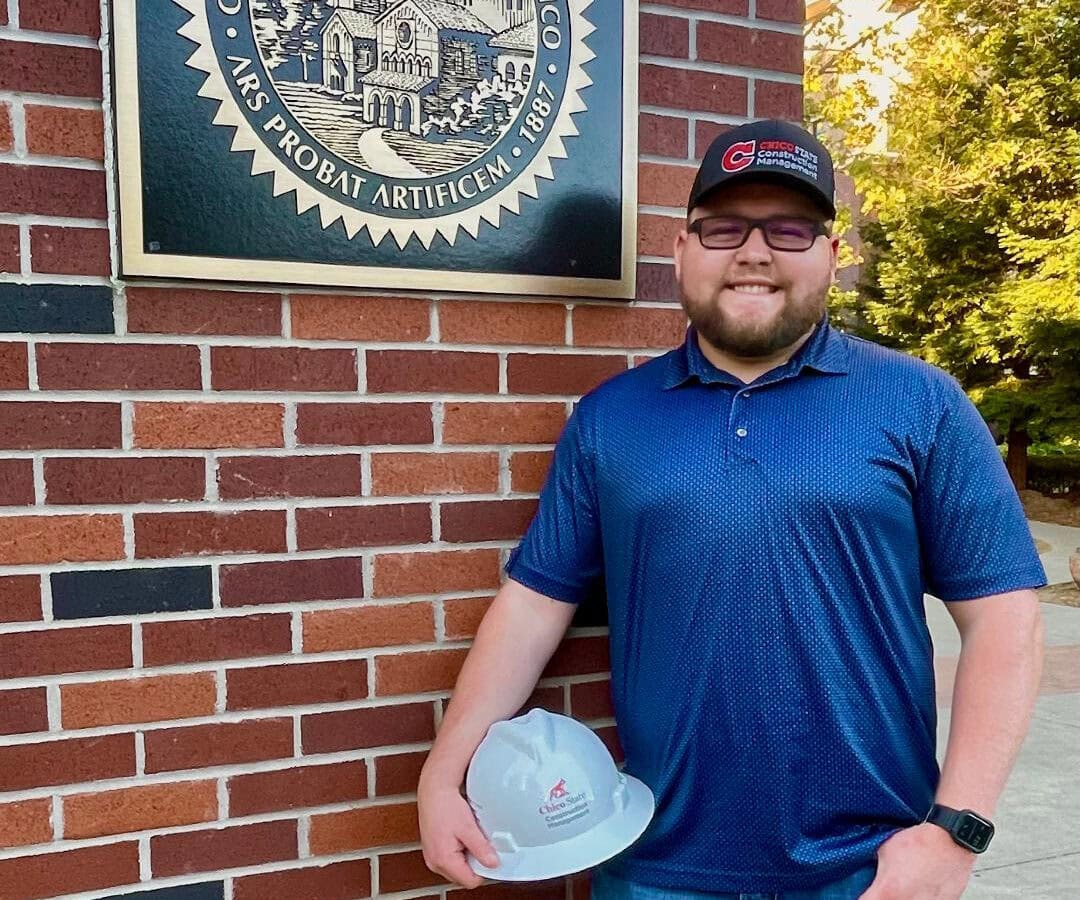 Man stands in front of brick wall holding a hard hat.