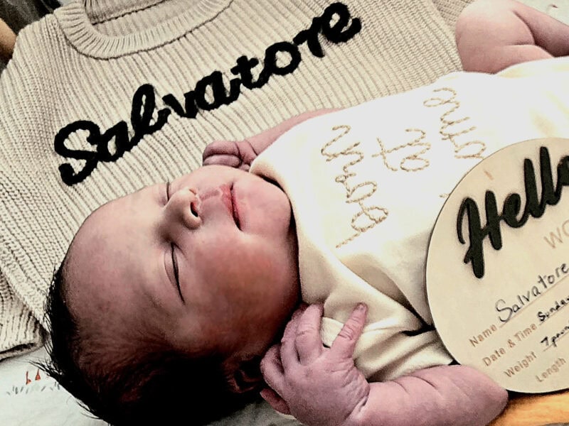 Baby sleeping in front of a sweater that says Salvatore.