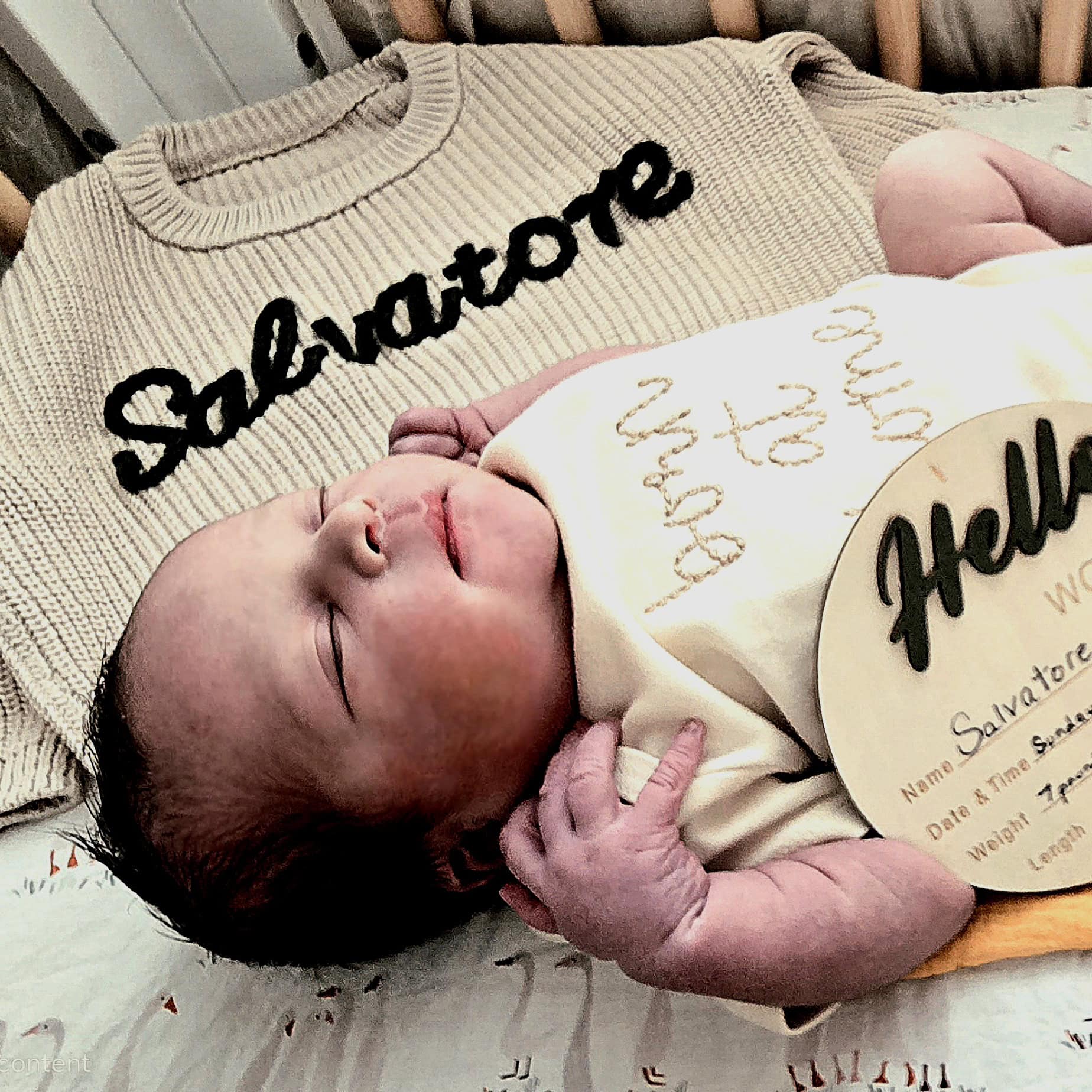 Baby sleeping in front of a sweater that says Salvatore.