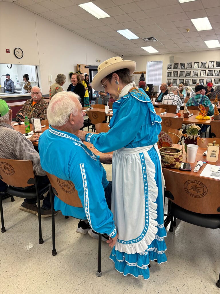 An elder helps another fix his Choctaw shirt.