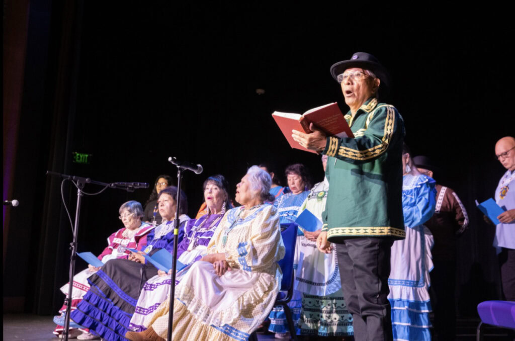 A man holds a book while singing Choctaw hymns.