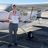 A young man poses for a photo in front of an airplane.