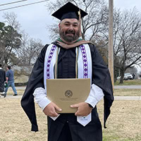 A man poses for a photo wearing a Choctaw graduation stole.