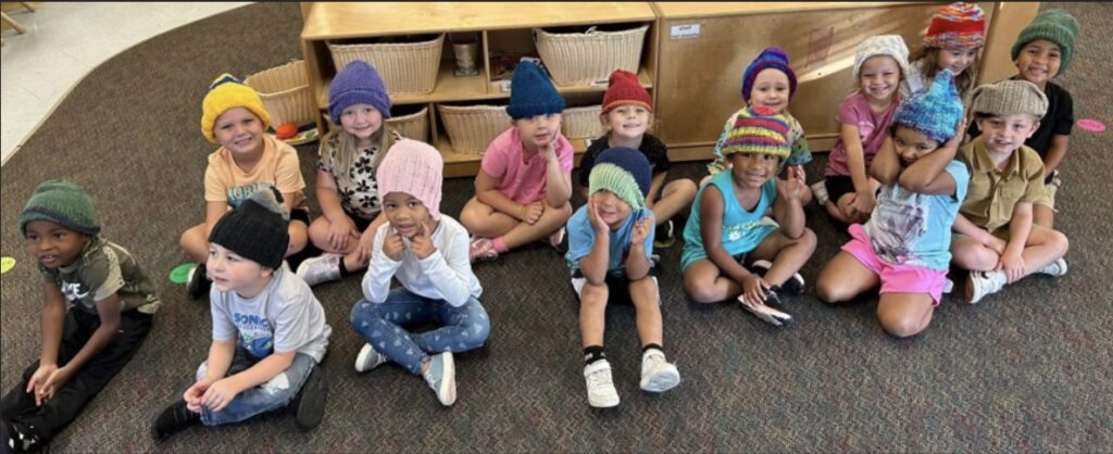 Children sit on the floor wearing knit hats.