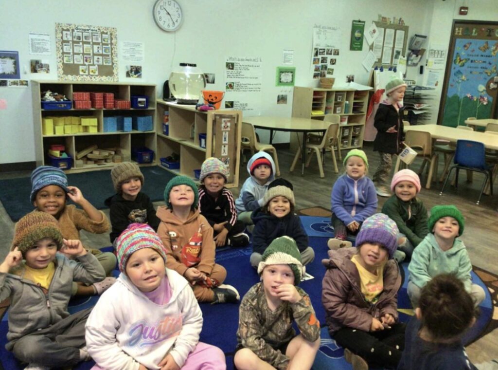 Children sit on the floor wearing knit hats.