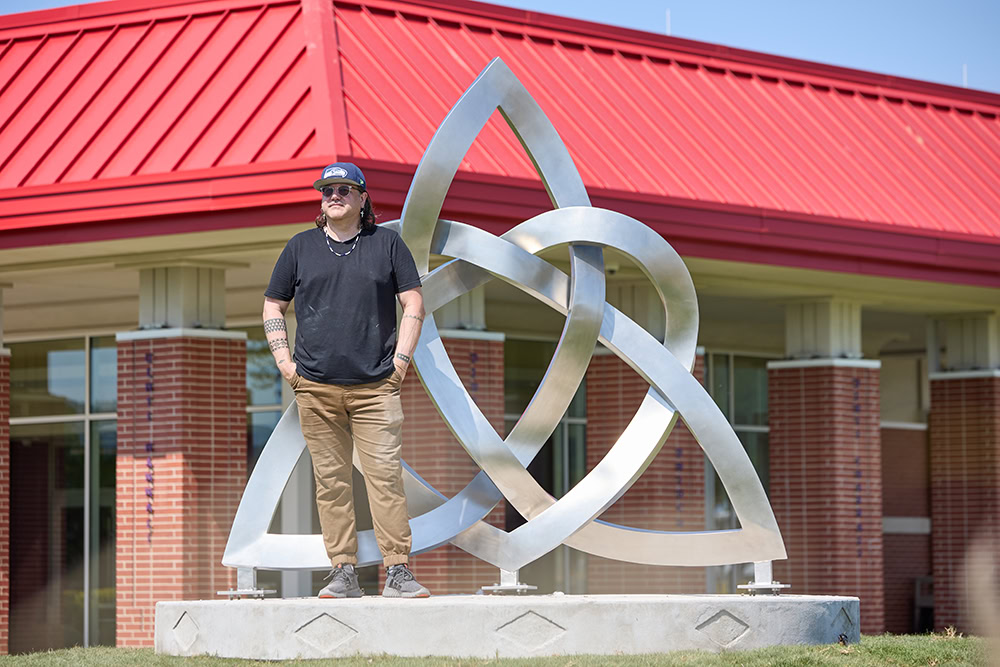 A man stands in front of a sculpture.