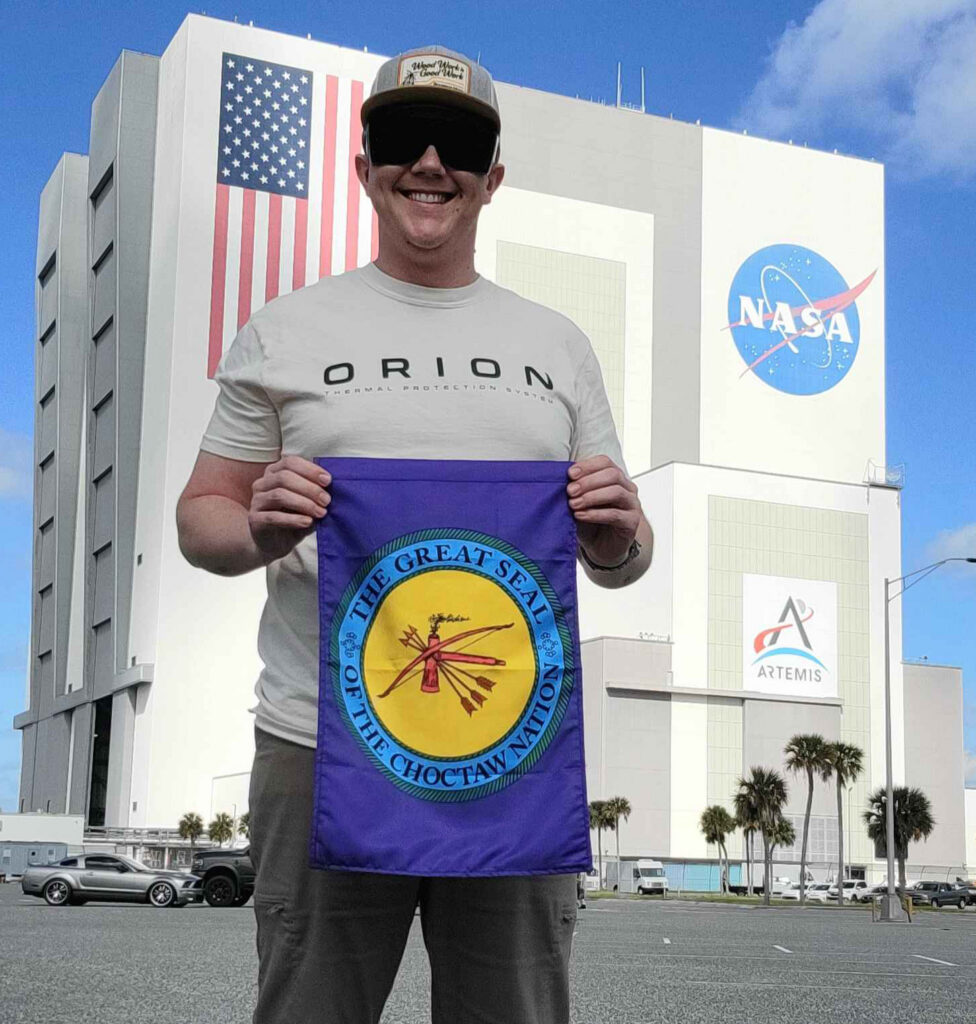 A man stands in front of ta NASA holding a Choctaw flag.