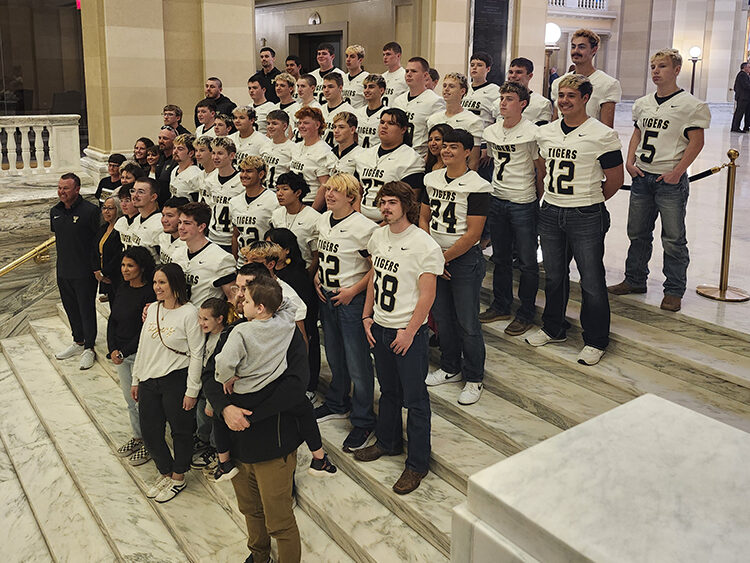 A group of young men wearing football jerseys stands on marble steps.