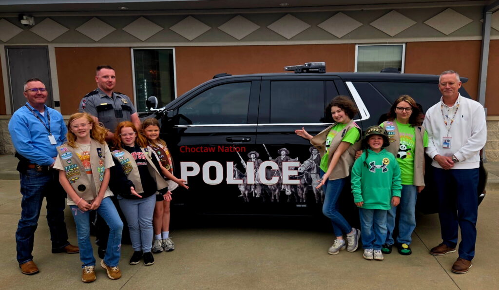 A group of Girls Scouts and policeman pose for a photo in front of a police car.