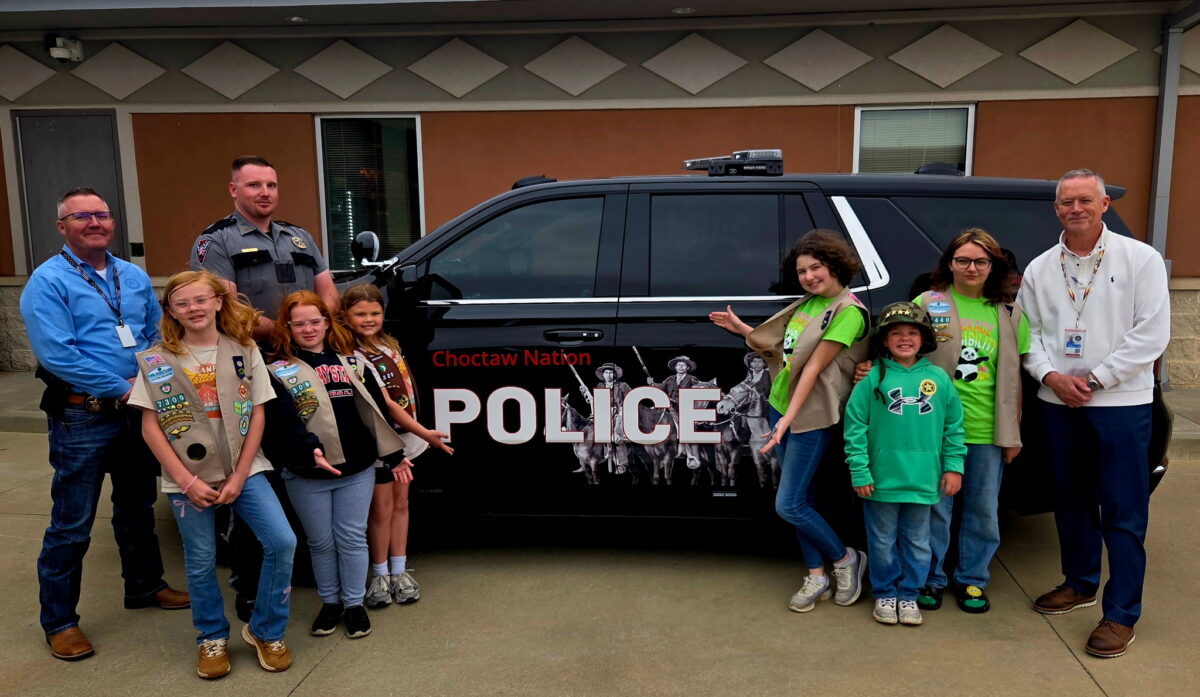 A group of Girls Scouts and policeman pose for a photo in front of a police car.