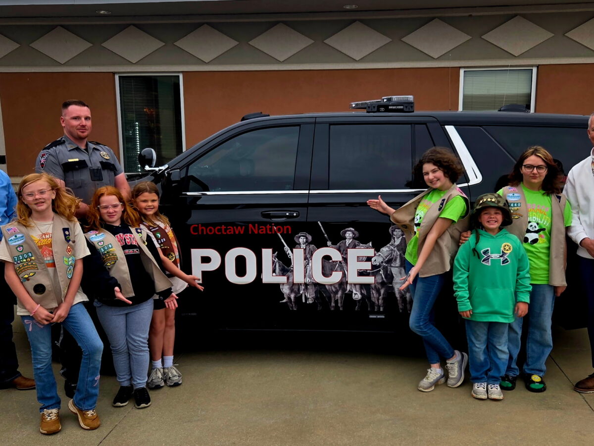 A group of Girls Scouts and policeman pose for a photo in front of a police car.