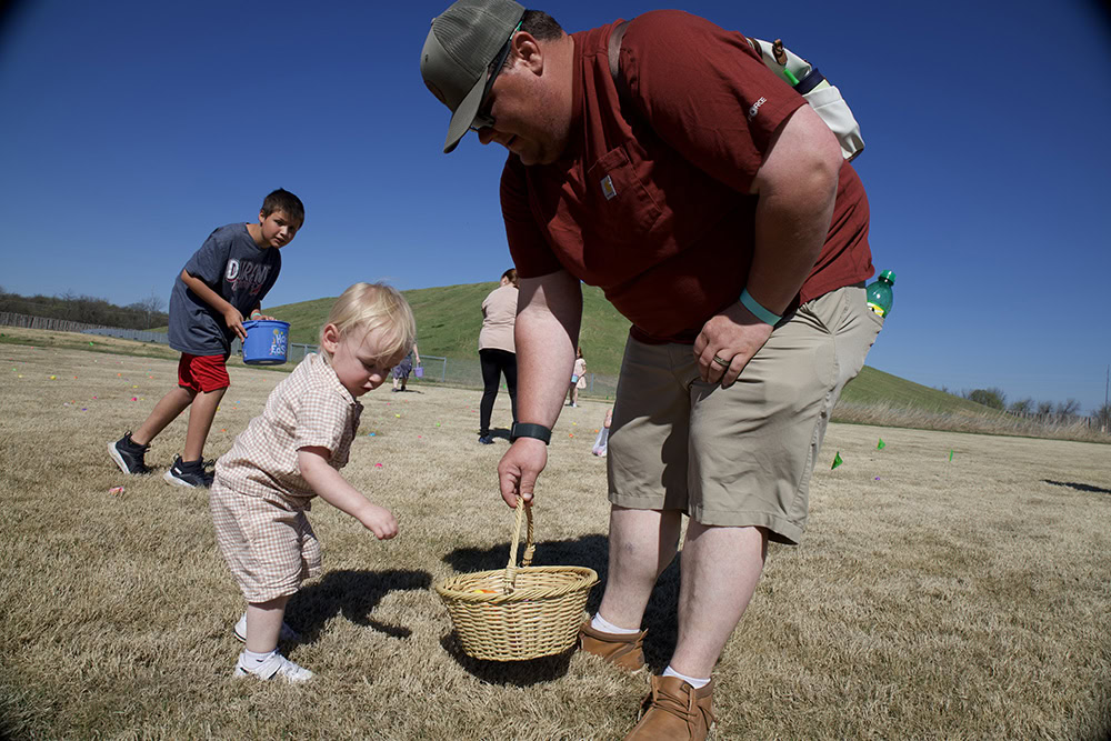 a parent helps a child gather Easter eggs.