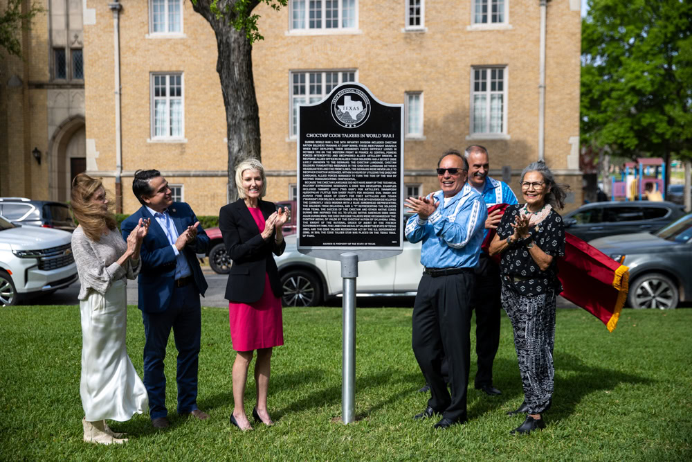 A group of people clap as a historical marker is unveiled.