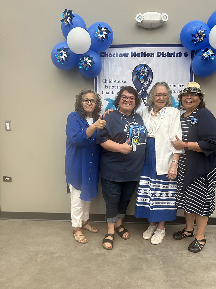 four women pose for a photo in front of a banner. 