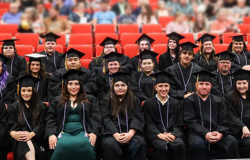 A large group of adults pose for a photo wearing graduation cap and gowns.