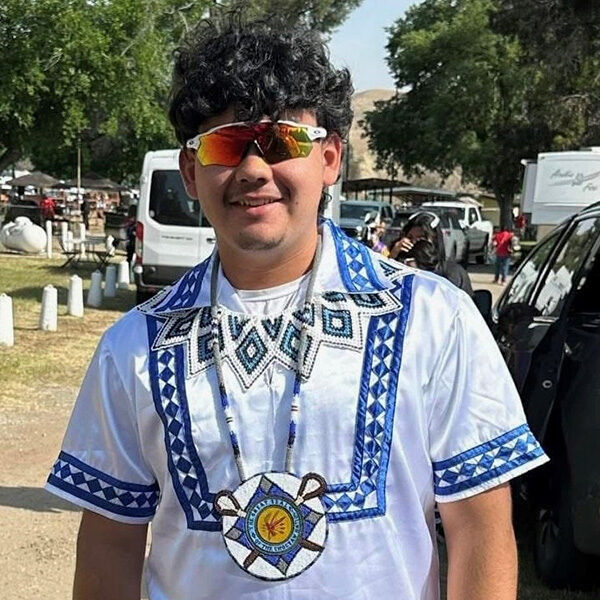 A young man poses for a photo wearing Native regalia.