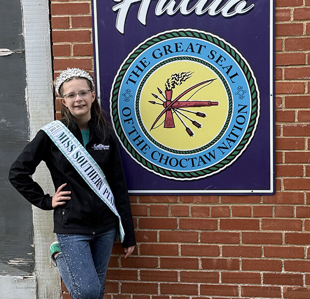 A young girls poses next to a sign with the seal of the Choctaw Nation on it.