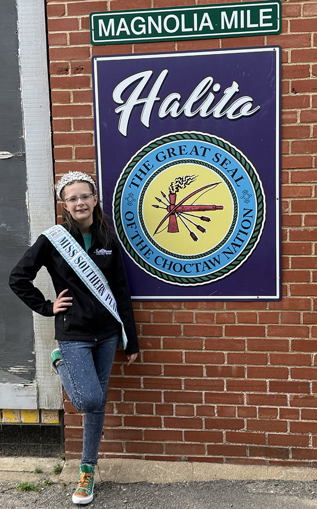 A young girls poses next to a sign with the seal of the Choctaw Nation on it.