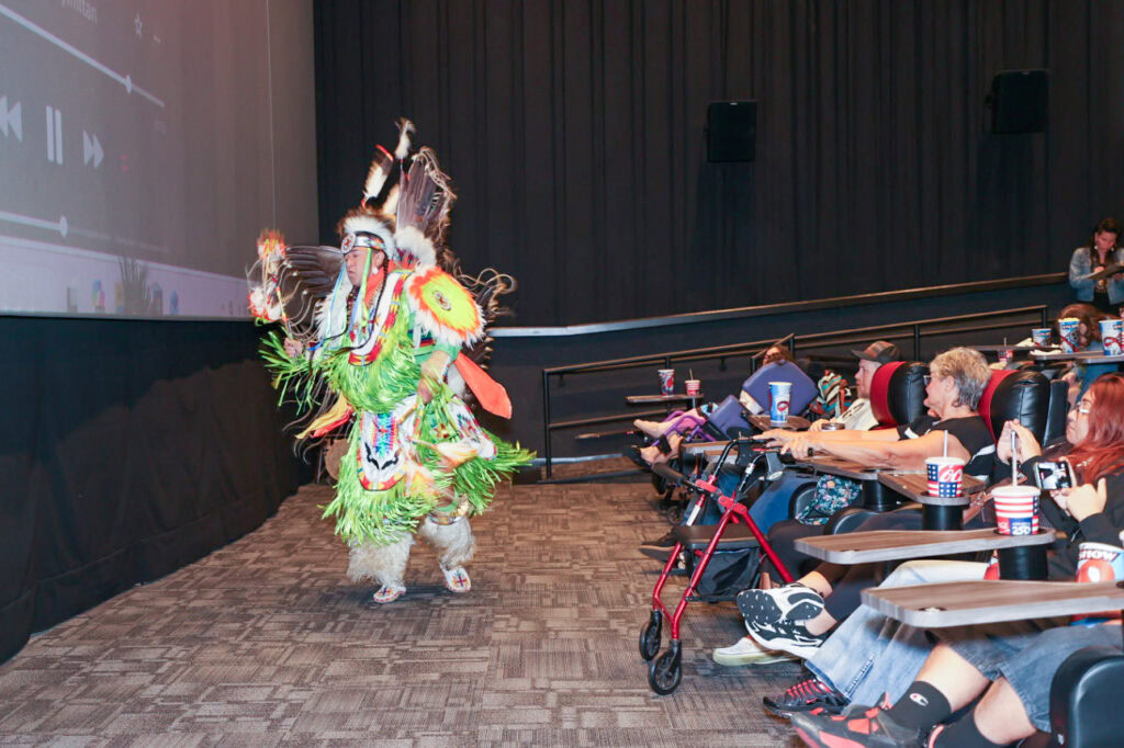 A man in traditional regalia dances in a theater.