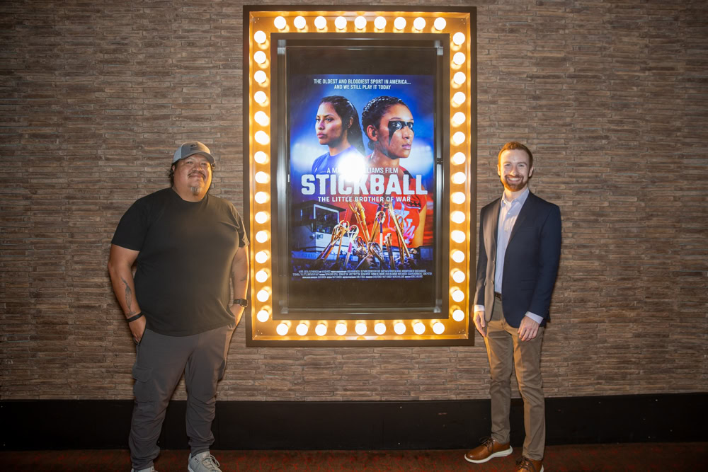 Two men pose for a photo next to a movie poster.
