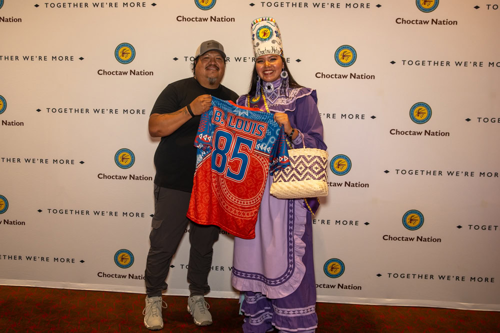 A man and a young women dressed in Choctaw princess regalia pose for a photo.