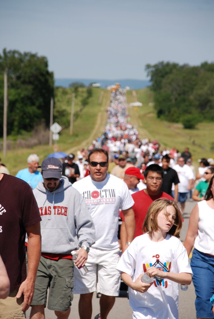 A large group of people walk down a road.