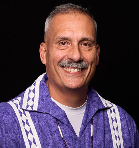 Assistant Chief smiles at the camera in a purple traditional Choctaw shirt.