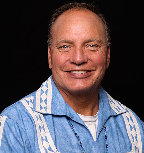 Chief Batton smiles while wearing a light blue traditional Choctaw shirt.