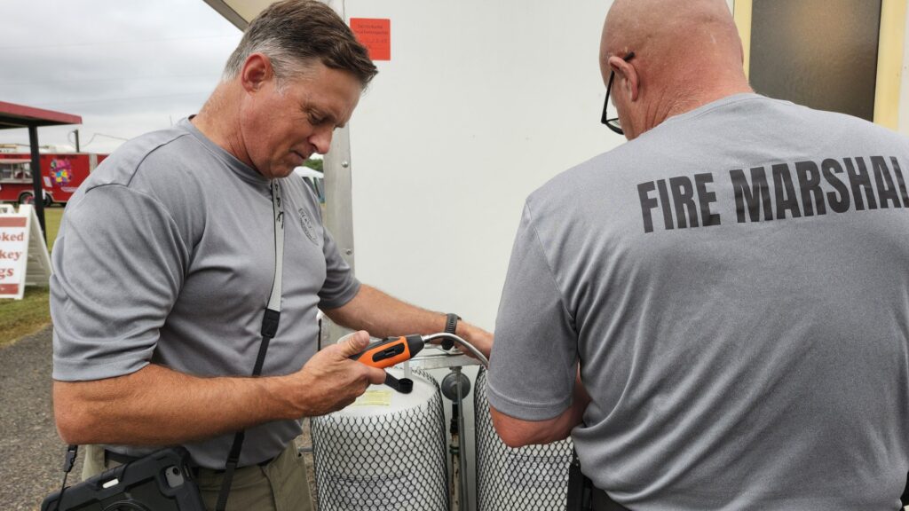 Two men wearing fire marshal shirts inspect a food truck.
