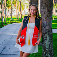 A young woman poses for a photo wearing a graduation stole.