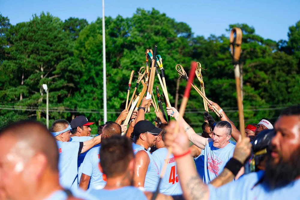 Stickball players raise their sticks.