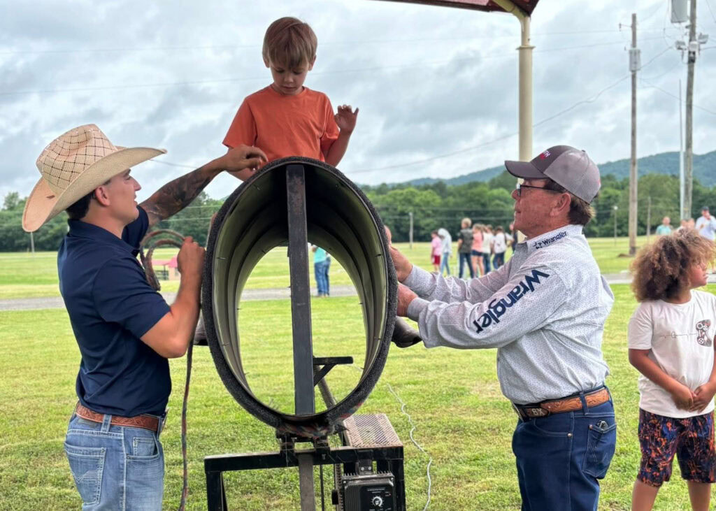 Camp volunteers help a young camper on a mechanical bull.