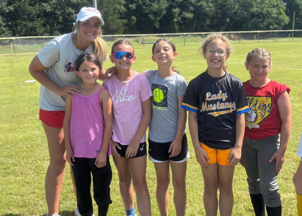 A camp volunteer poses for a photo with a group of softball campers.
