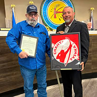 Two men pose for a photo one holding and award and the other holing a framed Choctaw veteran flag.