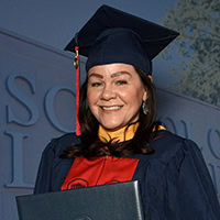 A woman poses for a photo wearing graduation regalia.