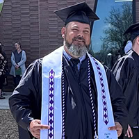 A man poses for a photo wearing graduation regalia.