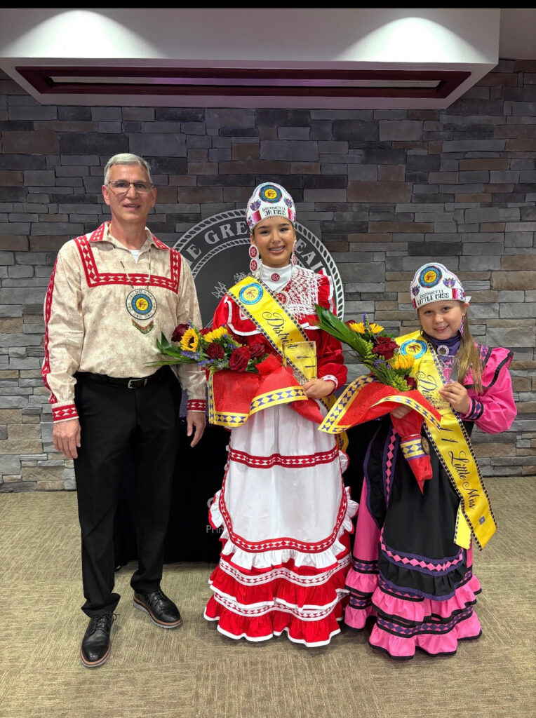 Two yonge girls in tribal regalia pose for a photo with tribal leadership.