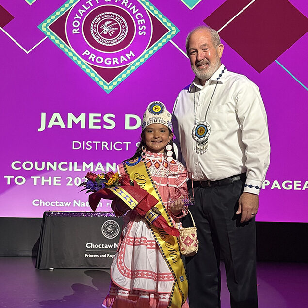 A man poses for a phot with a young girls wearing tribal regalia. 
