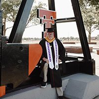 A man poses for a photo wearing graduation regalia.