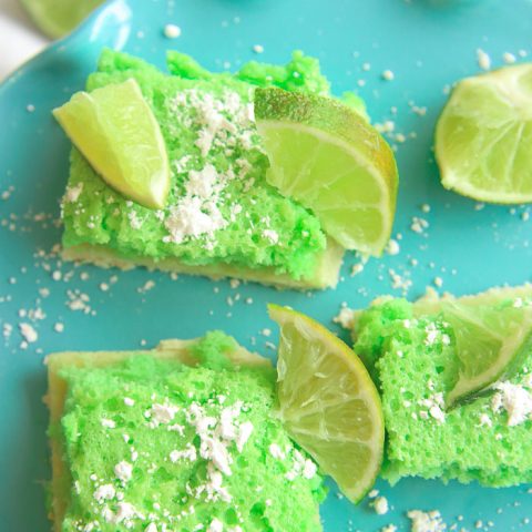 vertical close up of green gluten-free lime bars on a blue platter with powdered sugar and lime slices