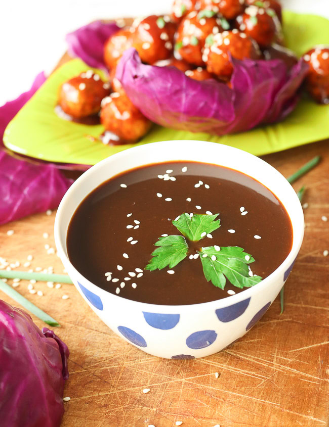 Bowl of hoisin sauce on a wooden plank, meatballs and vegetables in the background