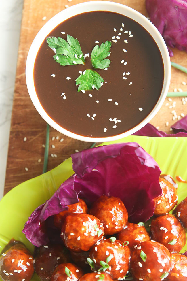 Top view of a bowl of sauce next to some salad and marinated meatballs