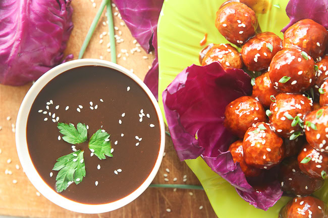 Top view of a bowl of sauce next to some salad and marinated meatballs