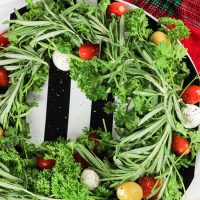 This holiday vegetable wreath is a festive holiday appetizer that is not only easy to put together, put easily adaptable to the party-goers likes and needs. Plate your favorite herbs underneath tasty mozzarella cheese, sweet tomatoes, and your favorite olives. Sprinkle cracked pepper and a delicious balsamic drizzle to finish!