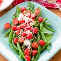 These 5 minute greek green beans use fresh cooked green beans that are drizzled with a quick homemade greek dressing and topped with fresh tomato and feta cheese crumbles. They are great served warm or cold and are perfect for all those summer parties!