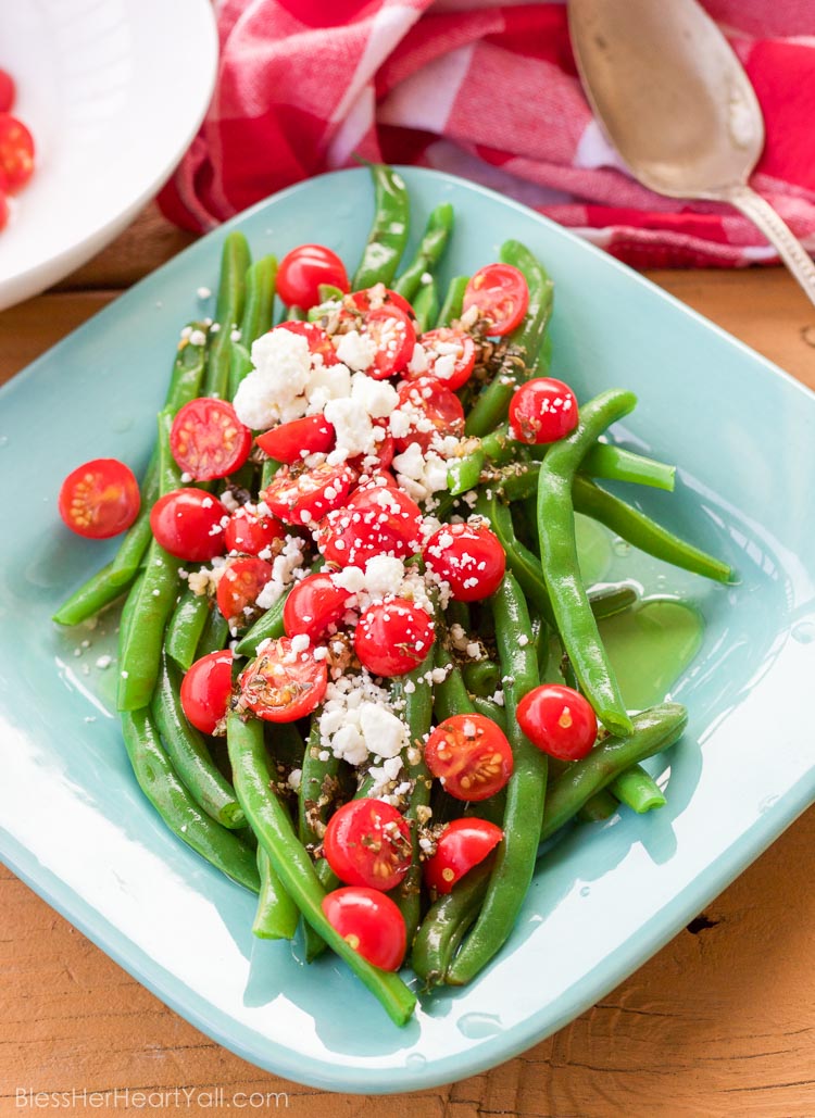 These 5 minute greek green beans use fresh cooked green beans that are drizzled with a quick homemade greek dressing and topped with fresh tomato and feta cheese crumbles. They are great served warm or cold and are perfect for all those summer parties!