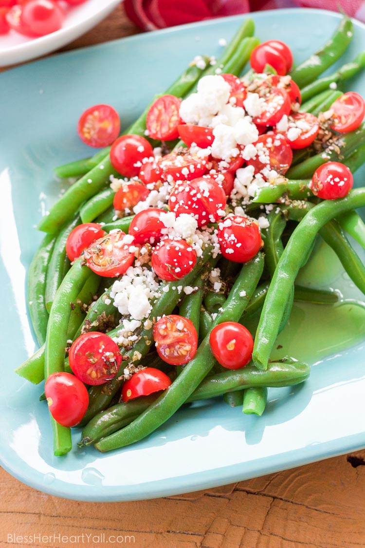 These 5 minute greek green beans use fresh cooked green beans that are drizzled with a quick homemade greek dressing and topped with fresh tomato and feta cheese crumbles. They are great served warm or cold and are perfect for all those summer parties!