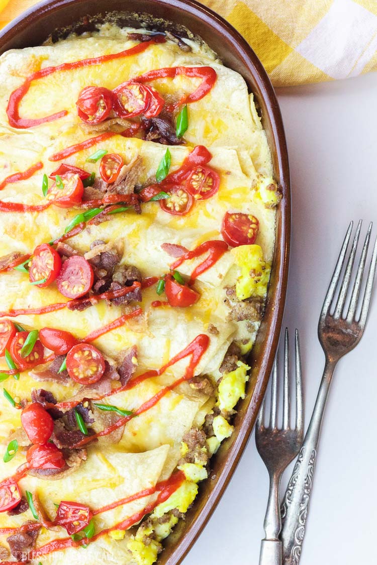 This delicious recipe for gluten-free breakfast enchiladas will wake anyone's taste buds up for the day! The combination of fluffy eggs and spicy breakfast sausage wrapped in corn tortillas and then topped with a seasoned cheese drizzle, baked and then loaded with fresh veggie chunks and bacon crumbles will make anyone's morning sunny!