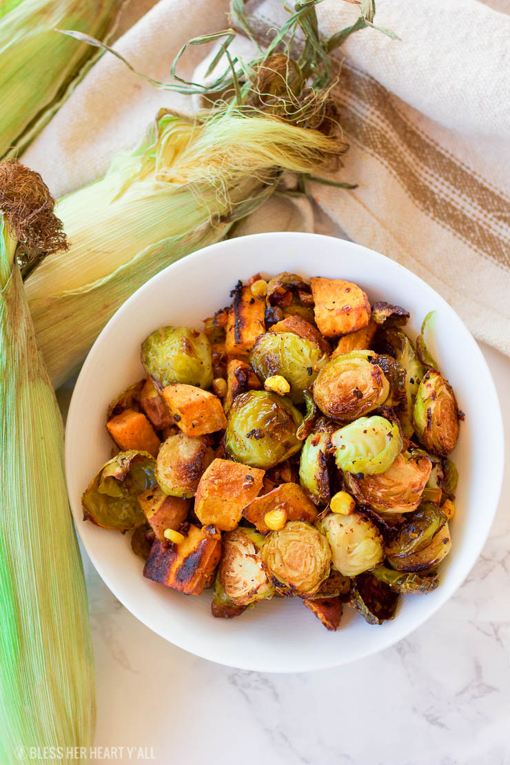 This healthy roasted sweet potato brussel sprout hash is a simple fall treat that drizzles on a light layer of olive oil, garlic, and cumin before roasting. The vegan and gluten-free recipe produces perfectly golden baked sweet potato pieces surrounded by fresh spiced corn kernels and crisp and tender cooked brussel sprouts.