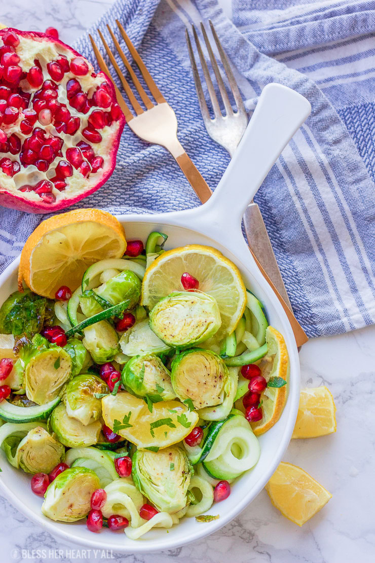 This roasted lemon garlic brussel sprouts + zucchini recipe is a clean, crisp, savory vegetable dish that is not only healthy but a gorgeous and easy addition to any meal! Lemon, honey, and garlic flavors coat the roasted brussel sprouts, zucchini noodles, and pomegranate arils for a colorful fresh salad.